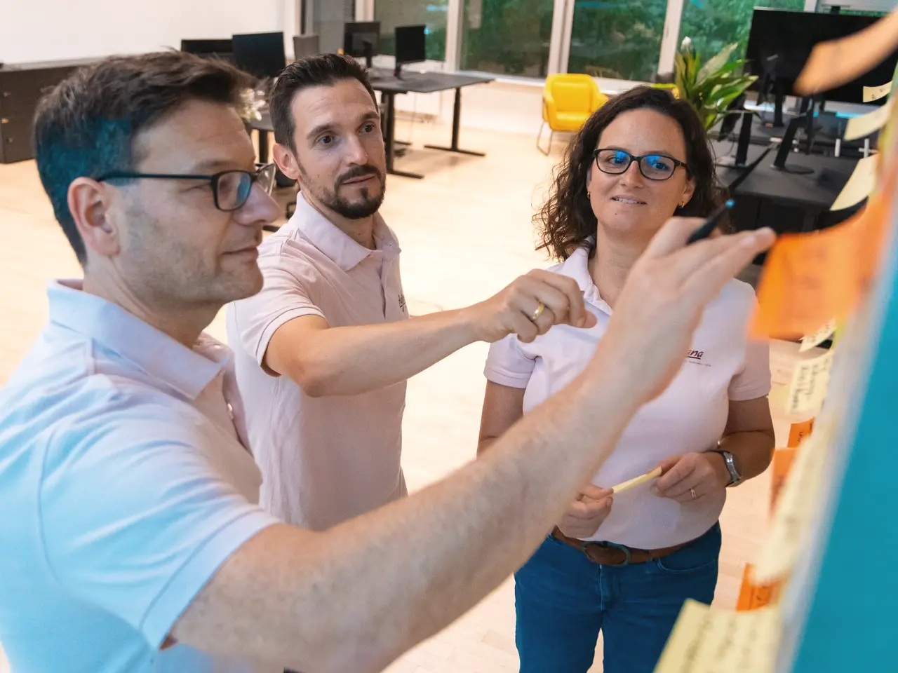 Drei Teilnehmende entwickeln gemeinsam Inhalte an einer Post-it-Wand.